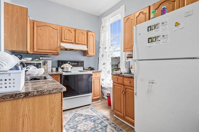 kitchen with dark countertops, white appliances, light wood-style floors, under cabinet range hood, and a sink