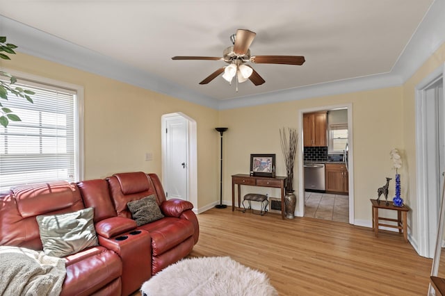 living room featuring light wood-type flooring, a ceiling fan, baseboards, and arched walkways