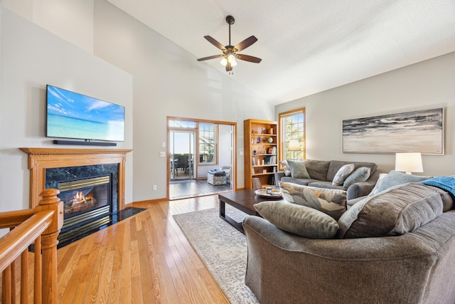 living area with baseboards, high vaulted ceiling, a high end fireplace, a ceiling fan, and light wood-style flooring