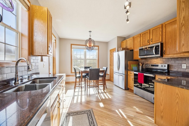 kitchen featuring a notable chandelier, appliances with stainless steel finishes, a sink, light wood-style flooring, and tasteful backsplash