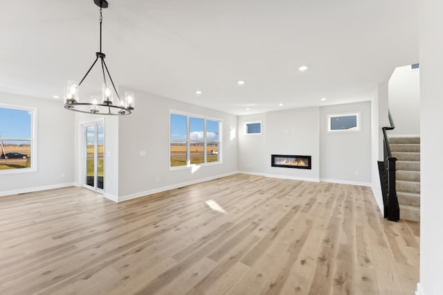 unfurnished living room with light wood-type flooring, stairs, plenty of natural light, a chandelier, and recessed lighting