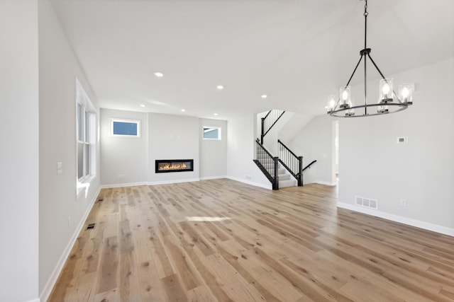 unfurnished living room featuring light wood-type flooring, stairway, a chandelier, recessed lighting, and a glass covered fireplace