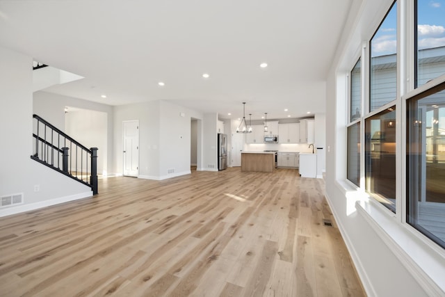 unfurnished living room with light wood-style flooring, stairway, baseboards, recessed lighting, and healthy amount of natural light