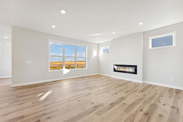 unfurnished living room featuring light wood finished floors, a glass covered fireplace, baseboards, and recessed lighting