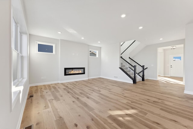 unfurnished living room with stairway, light wood-style flooring, plenty of natural light, and recessed lighting