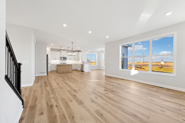 unfurnished living room with baseboards, light wood-style flooring, recessed lighting, a chandelier, and stairs