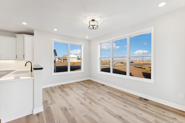 unfurnished dining area featuring a sink, light wood-style flooring, recessed lighting, and baseboards