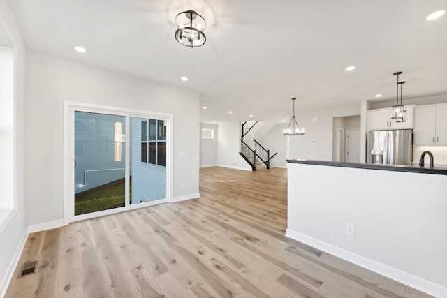unfurnished living room featuring recessed lighting, light wood-style flooring, a chandelier, baseboards, and stairway