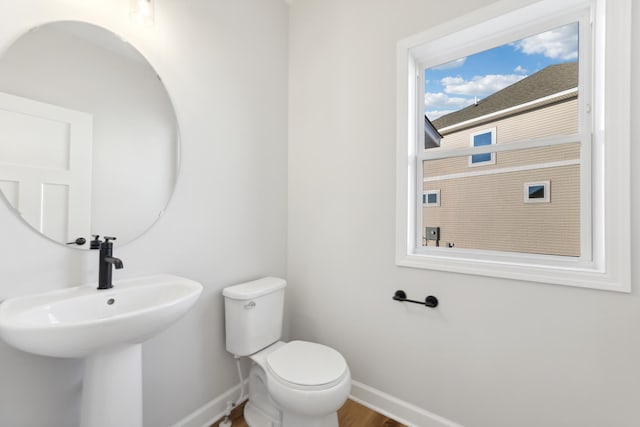 half bath with baseboards, toilet, a sink, and wood finished floors