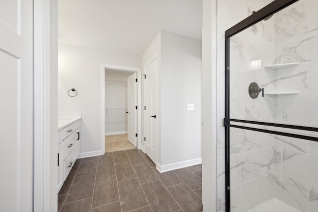 full bathroom with a shower stall, vanity, a spacious closet, and baseboards