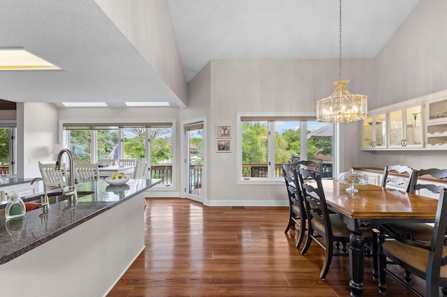 dining space with a high ceiling, dark wood-style flooring, a chandelier, and baseboards