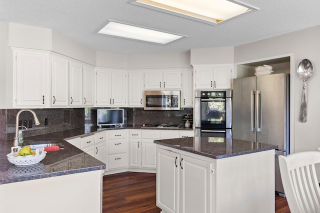 kitchen with stainless steel appliances, a sink, dark wood-type flooring, dark stone countertops, and a textured ceiling