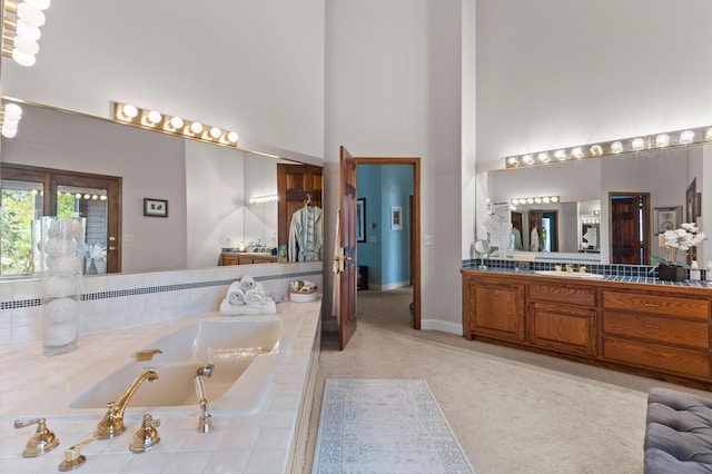 bathroom with a high ceiling, vanity, a bath, and baseboards