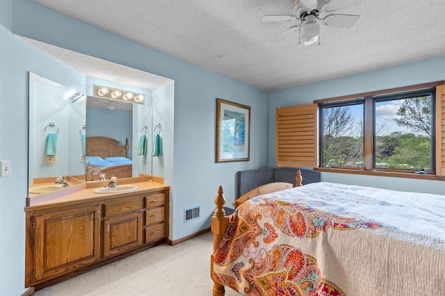 bedroom featuring a sink, a textured ceiling, light colored carpet, baseboards, and a ceiling fan