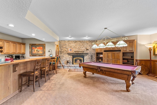 rec room featuring a textured ceiling, light carpet, billiards, a wainscoted wall, and a fireplace