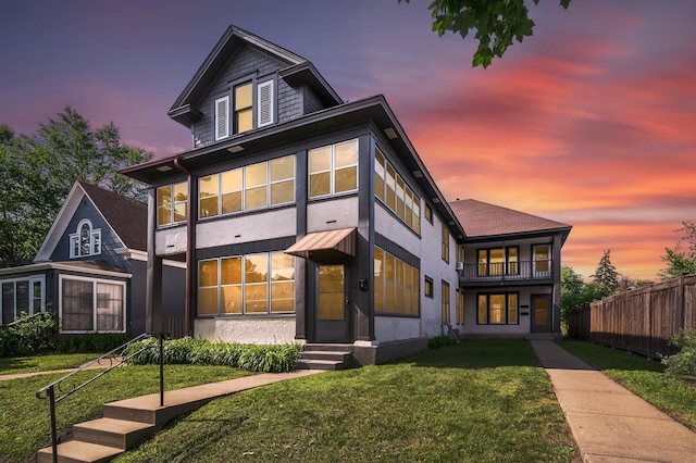 view of front of house with fence, a balcony, a front yard, and stucco siding