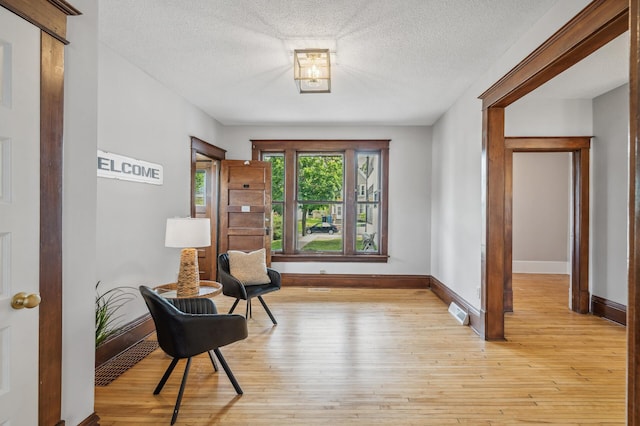 living area with baseboards, a textured ceiling, visible vents, and light wood-type flooring