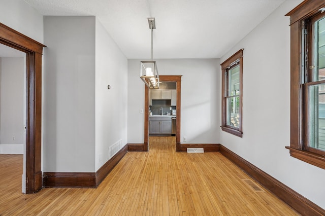 unfurnished dining area featuring baseboards, visible vents, and light wood-style flooring