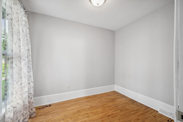 unfurnished room with baseboards, a textured ceiling, wood finished floors, and visible vents