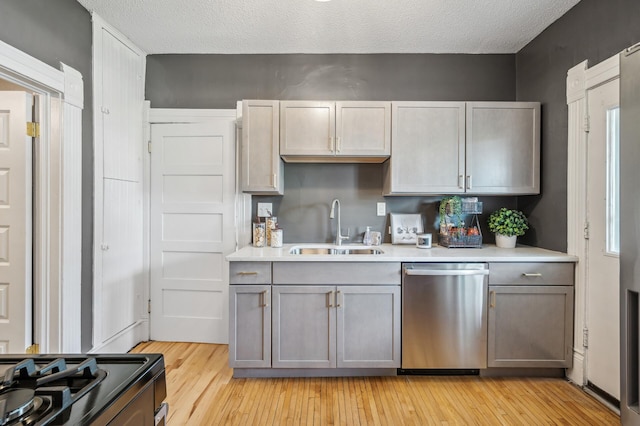 kitchen with gray cabinets, stainless steel dishwasher, a sink, light countertops, and light wood-style flooring