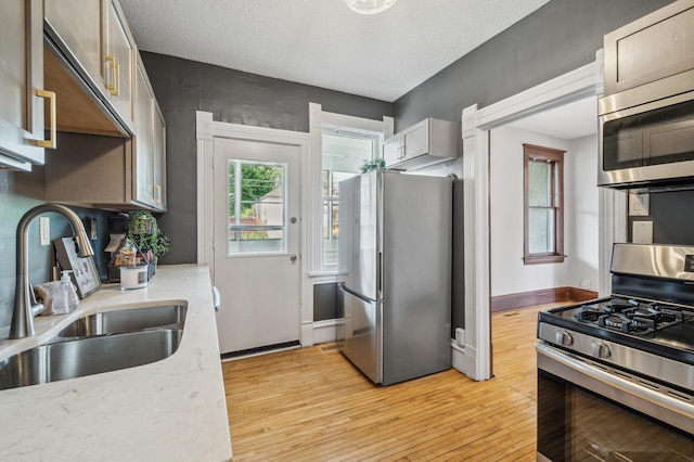 kitchen with light stone countertops, light wood-type flooring, a textured ceiling, a sink, and appliances with stainless steel finishes