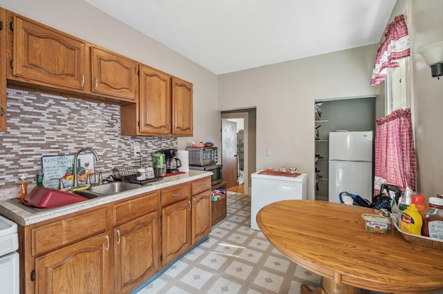 kitchen with a sink, light countertops, light floors, freestanding refrigerator, and tasteful backsplash