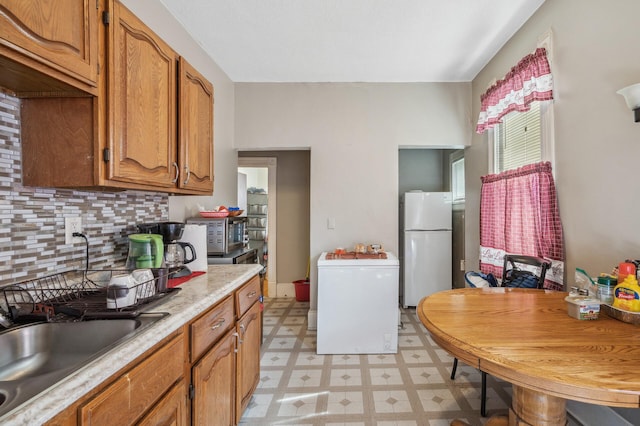 kitchen featuring light countertops, freestanding refrigerator, light floors, backsplash, and refrigerator