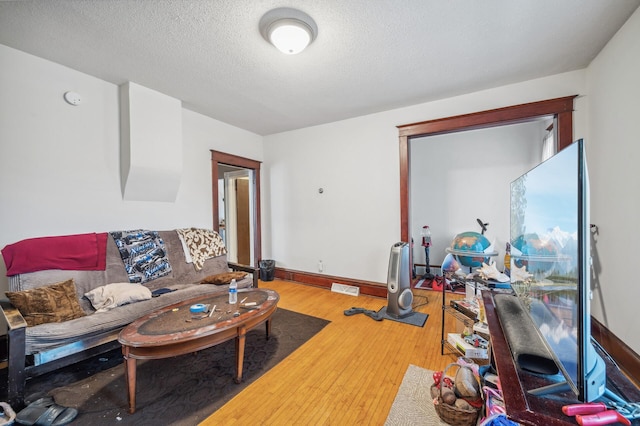 living room featuring a textured ceiling, visible vents, baseboards, and hardwood / wood-style flooring