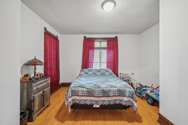 bedroom with light wood-style floors, a textured ceiling, and baseboards
