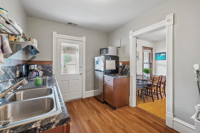 kitchen featuring visible vents, freestanding refrigerator, dark countertops, white microwave, and a sink