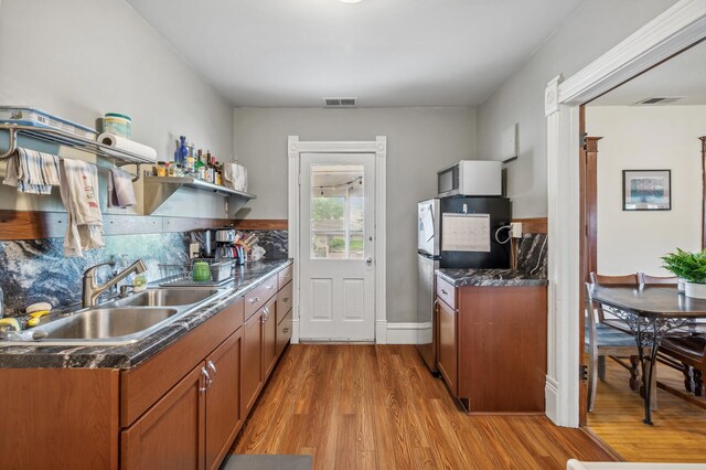 kitchen featuring brown cabinets, a sink, light wood-style flooring, white microwave, and visible vents