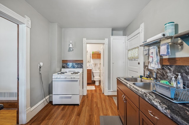 kitchen featuring wood finished floors, a sink, decorative backsplash, and white range with gas stovetop