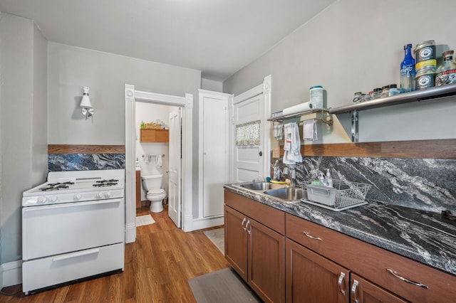 kitchen with brown cabinetry, open shelves, a sink, white gas range oven, and light wood-style flooring