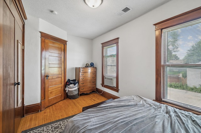 bedroom featuring a textured ceiling, visible vents, wood finished floors, baseboards, and cooling unit