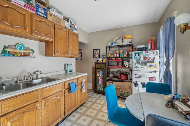 kitchen with freestanding refrigerator, light floors, light countertops, brown cabinets, and a sink