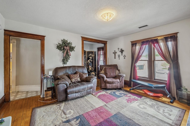 living area featuring baseboards, a textured ceiling, visible vents, and hardwood / wood-style floors