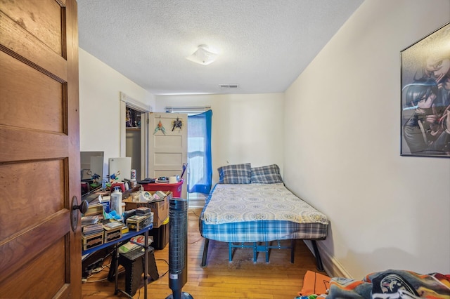 bedroom with baseboards, hardwood / wood-style flooring, a textured ceiling, and visible vents