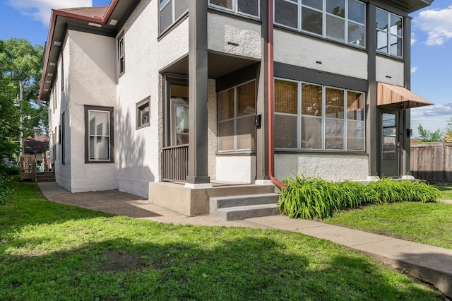 property entrance featuring a lawn, stucco siding, and fence