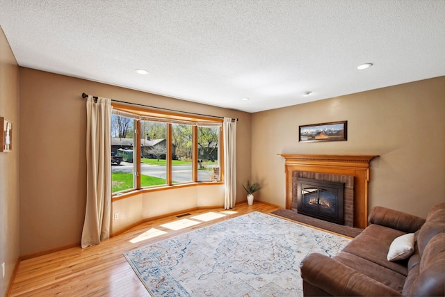living area featuring visible vents, a brick fireplace, baseboards, light wood-type flooring, and a textured ceiling