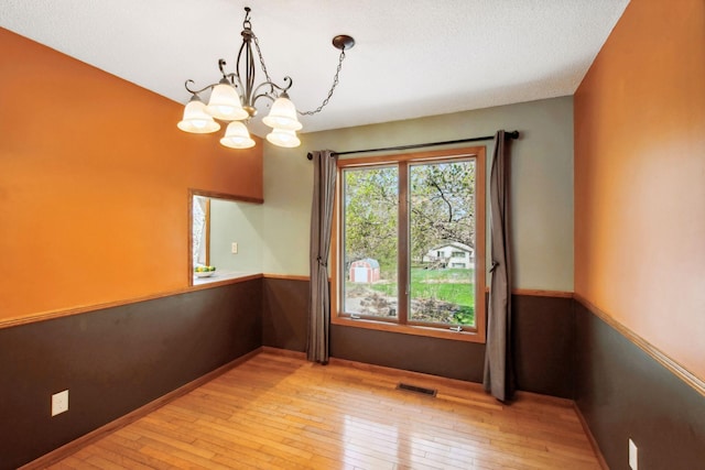 unfurnished dining area with a notable chandelier, visible vents, baseboards, and light wood-type flooring