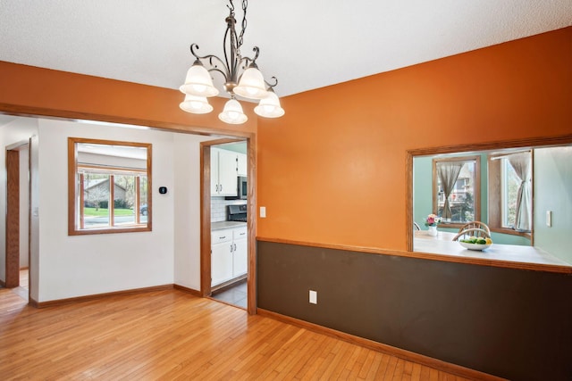 spare room with baseboards, an inviting chandelier, and light wood finished floors
