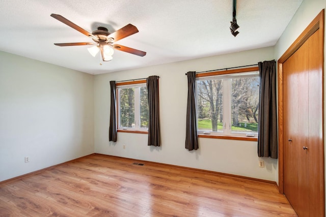 spare room with visible vents, baseboards, light wood-type flooring, rail lighting, and a ceiling fan