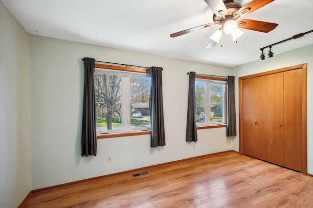 unfurnished bedroom with track lighting, baseboards, wood finished floors, visible vents, and a closet