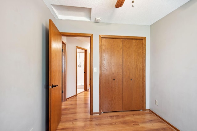 unfurnished bedroom featuring a closet, light wood-style floors, baseboards, ceiling fan, and a textured ceiling