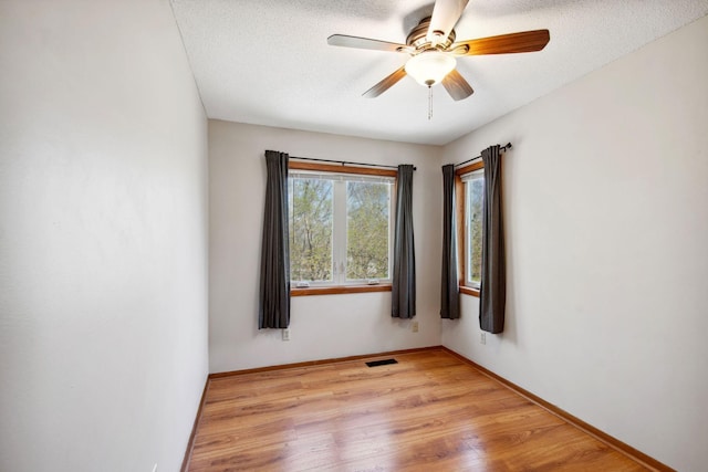 empty room with a ceiling fan, a textured ceiling, visible vents, baseboards, and light wood finished floors