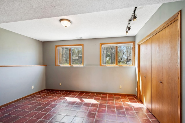 tiled spare room with track lighting, a textured ceiling, baseboards, and visible vents