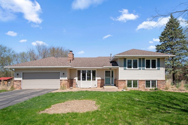split level home with an attached garage, brick siding, a front yard, a chimney, and driveway