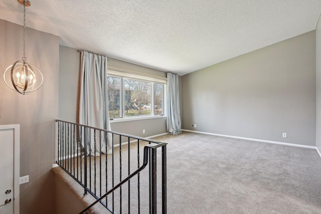 carpeted spare room featuring baseboards, a textured ceiling, and a notable chandelier