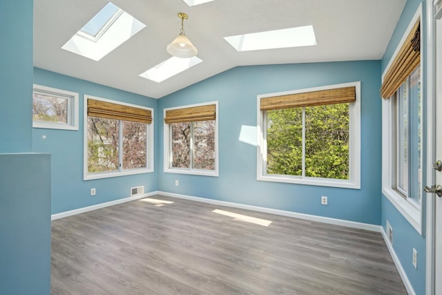 spare room featuring baseboards, visible vents, wood finished floors, and vaulted ceiling with skylight