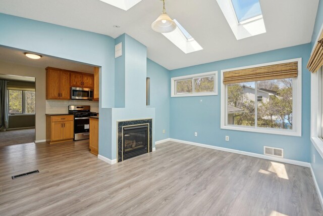 unfurnished living room featuring a skylight, visible vents, light wood-style floors, and a high end fireplace